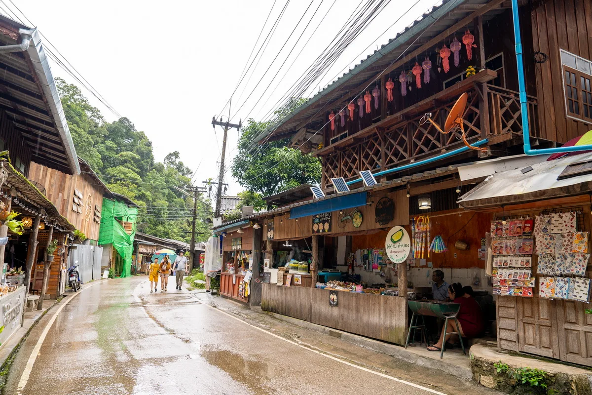 Wet asphalt lane lined with wooden houses and Lanna lanterns after rain in Mae Kampong Village