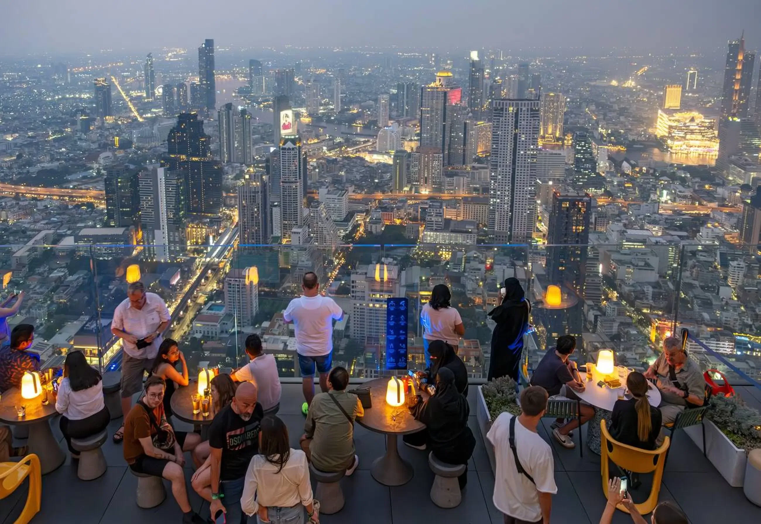 Crowded Mahanakhon SkyWalk outdoor deck at twilight over Bangkok city lights