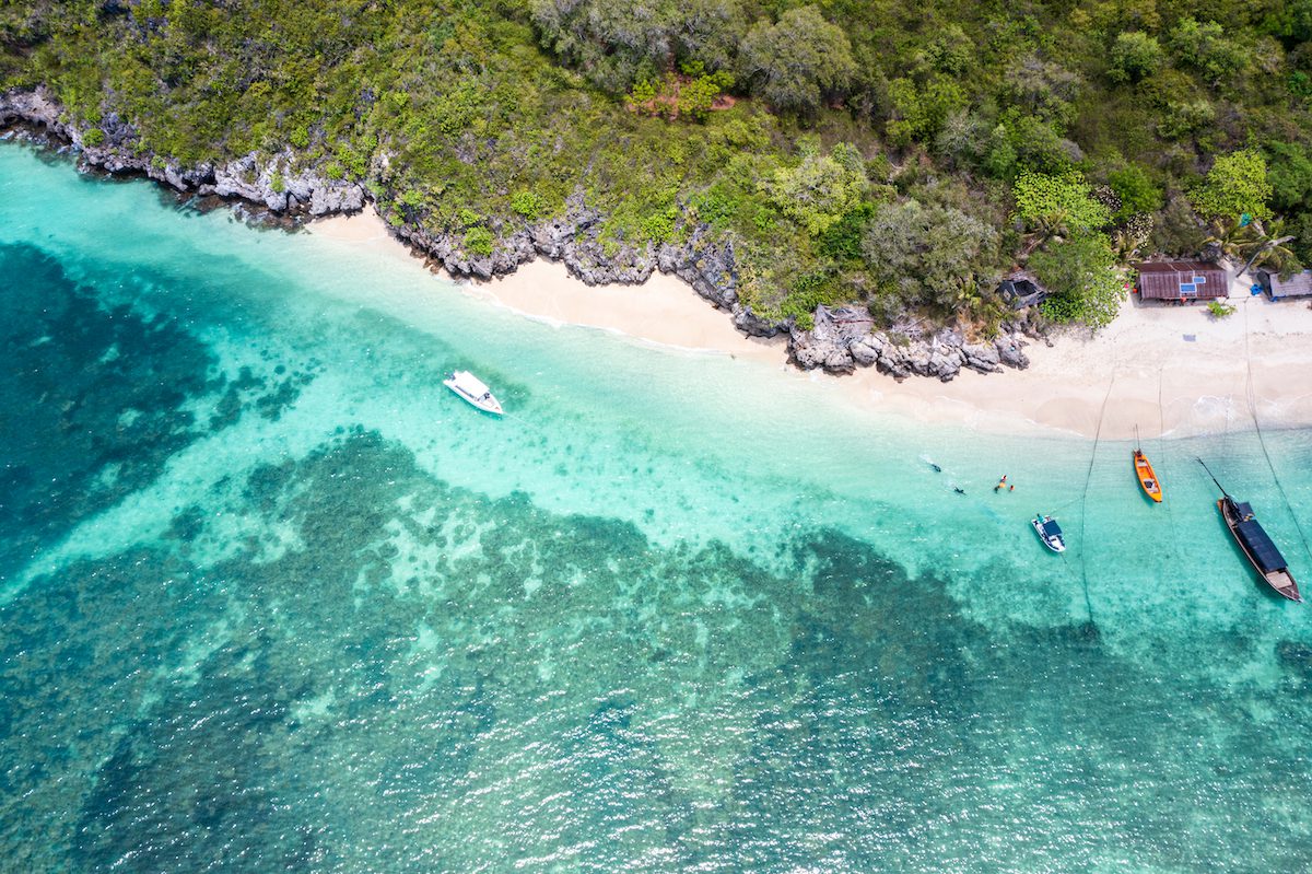 Overhead view of a sandy cove, boats and reef shallows along Hat Wanakon’s island coast