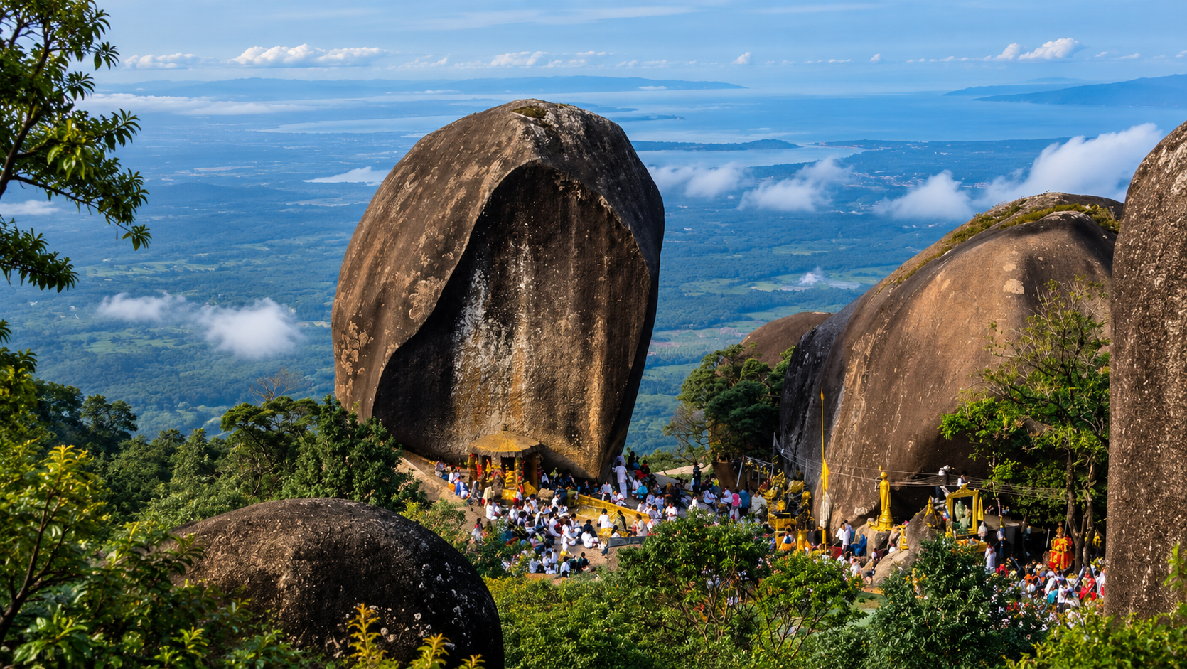 Pilgrims gathered among giant granite boulders at Phra Bat Phluang, with the Gulf of Thailand in the distance