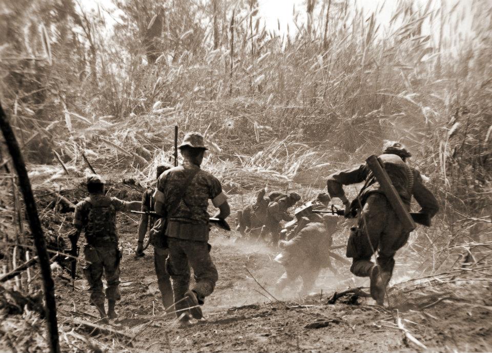 Historical photograph of soldiers advancing through tall grass during Thailand’s insurgency era