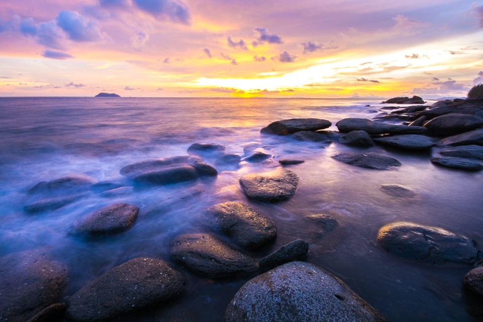 Sunset over a rocky Andaman shore, with a small island on the horizon at Laem Son National Park