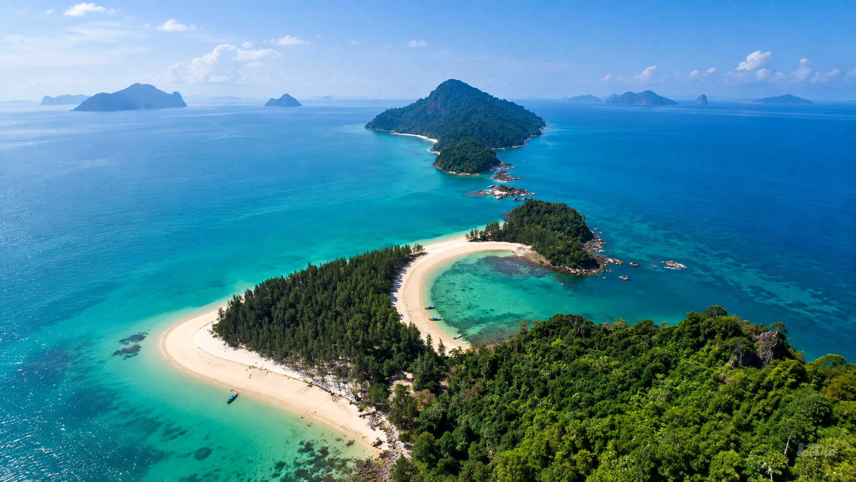 Aerial view of a forested island and curved sandy spit in turquoise water in the Laem Son island landscape