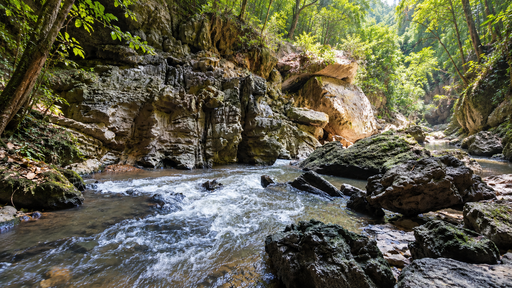 A forest stream cutting through mossy limestone cliffs and boulders at Lam Khlong Ngu National Park