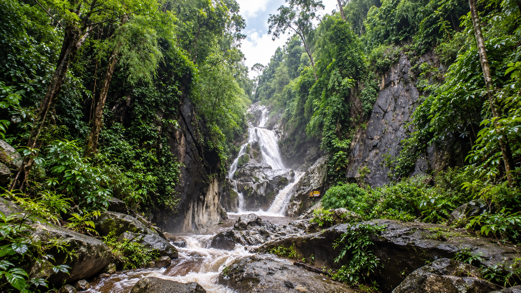 A multi-tiered waterfall dropping between dark cliffs and dense forest at Lan Sang National Park
