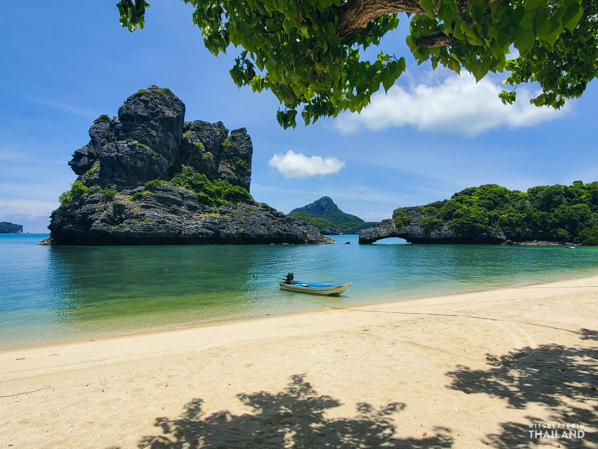 Sandy beach, longtail boat and a limestone stack with a natural stone arch in Mu Ko Ang Thong National Park