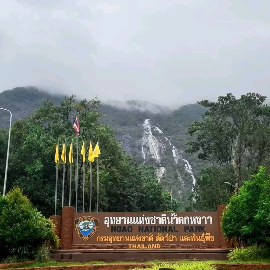 Park entrance sign with Ngao Waterfall visible as a white ribbon on the misty mountain behind