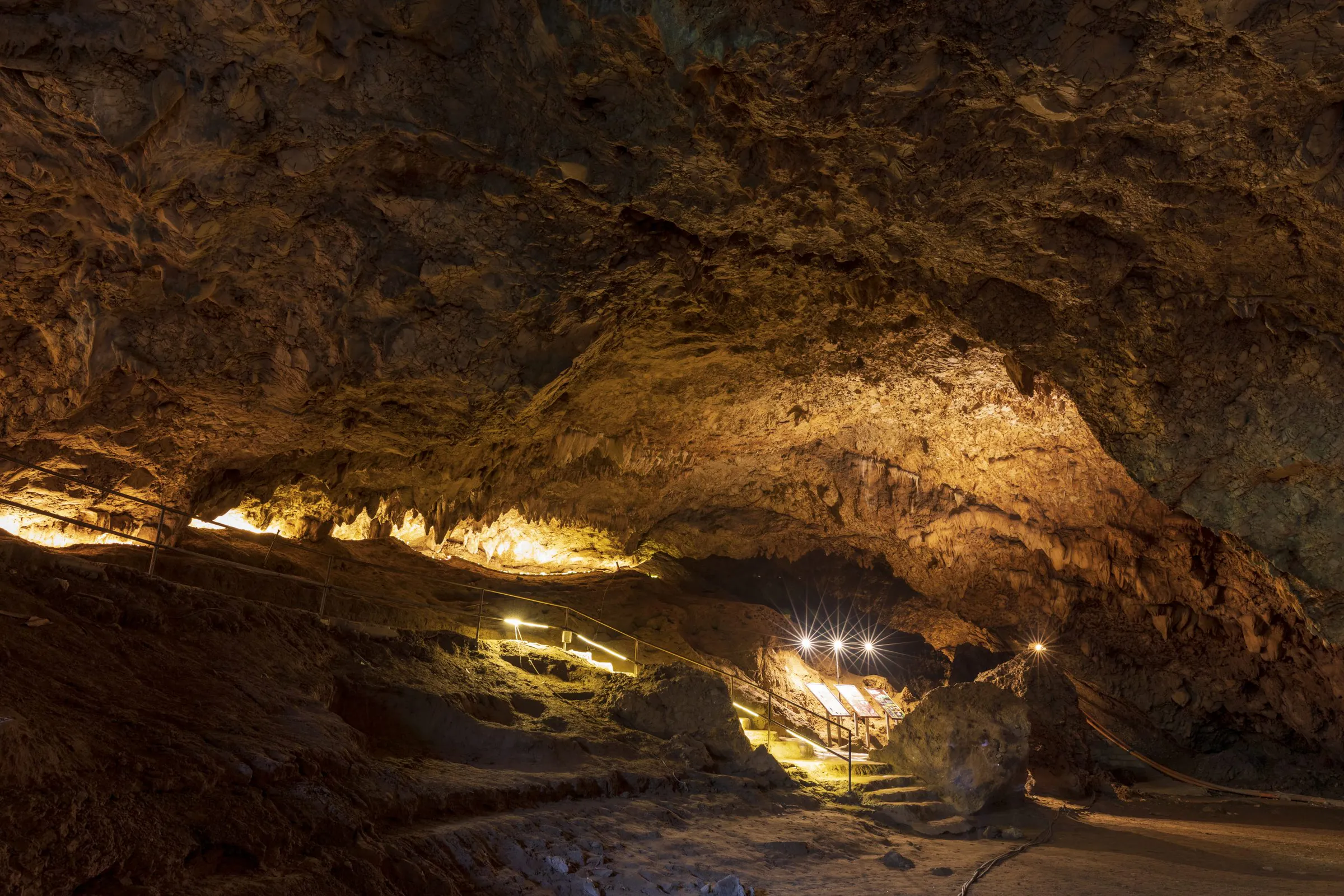 Lit limestone passage inside Tham Luang Cave, with railings and steps beneath a rugged ceiling in Mae Sai, Chiang Rai