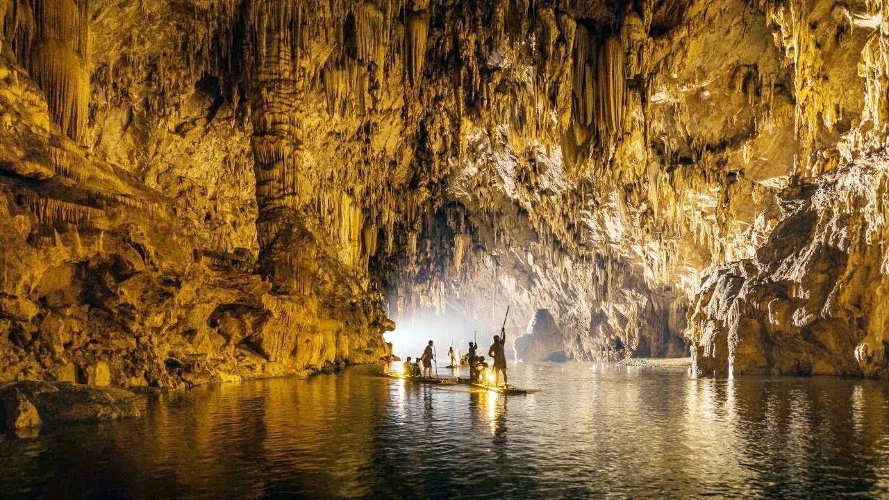 Visitors on wooden rafts moving through a floodlit limestone cave chamber with dense stalactites at Tham Luang–Khun Nam Nang Non, Chiang Rai