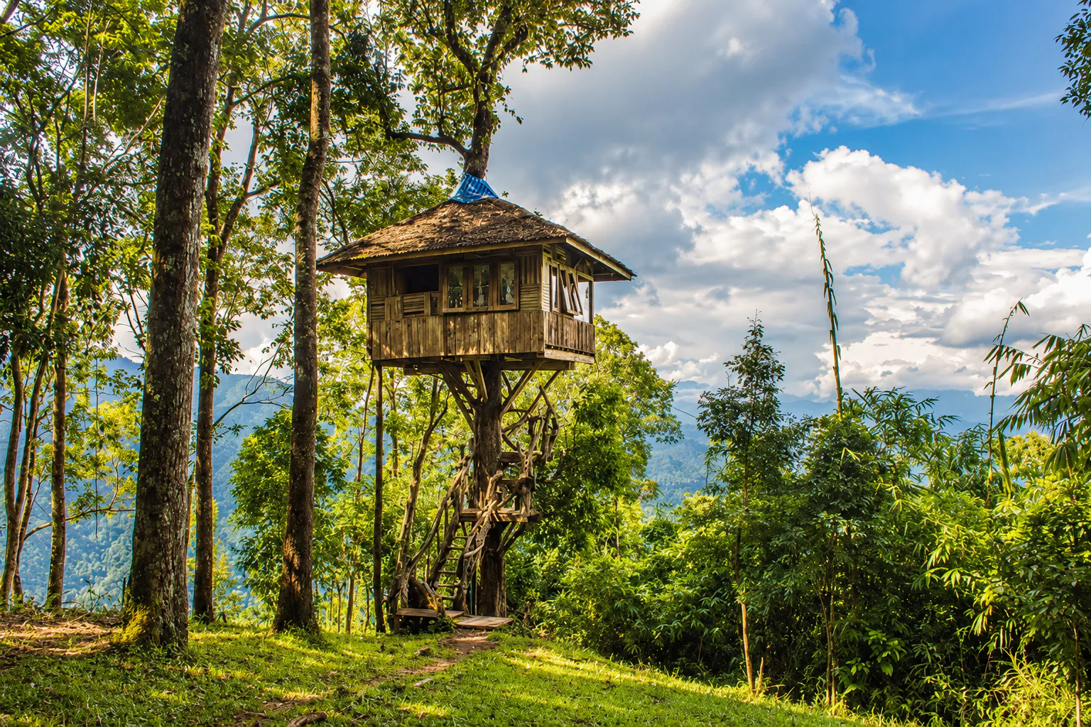 A wooden treehouse on stilts in highland forest at Thong Pha Phum National Park, with mountains beyond the trees