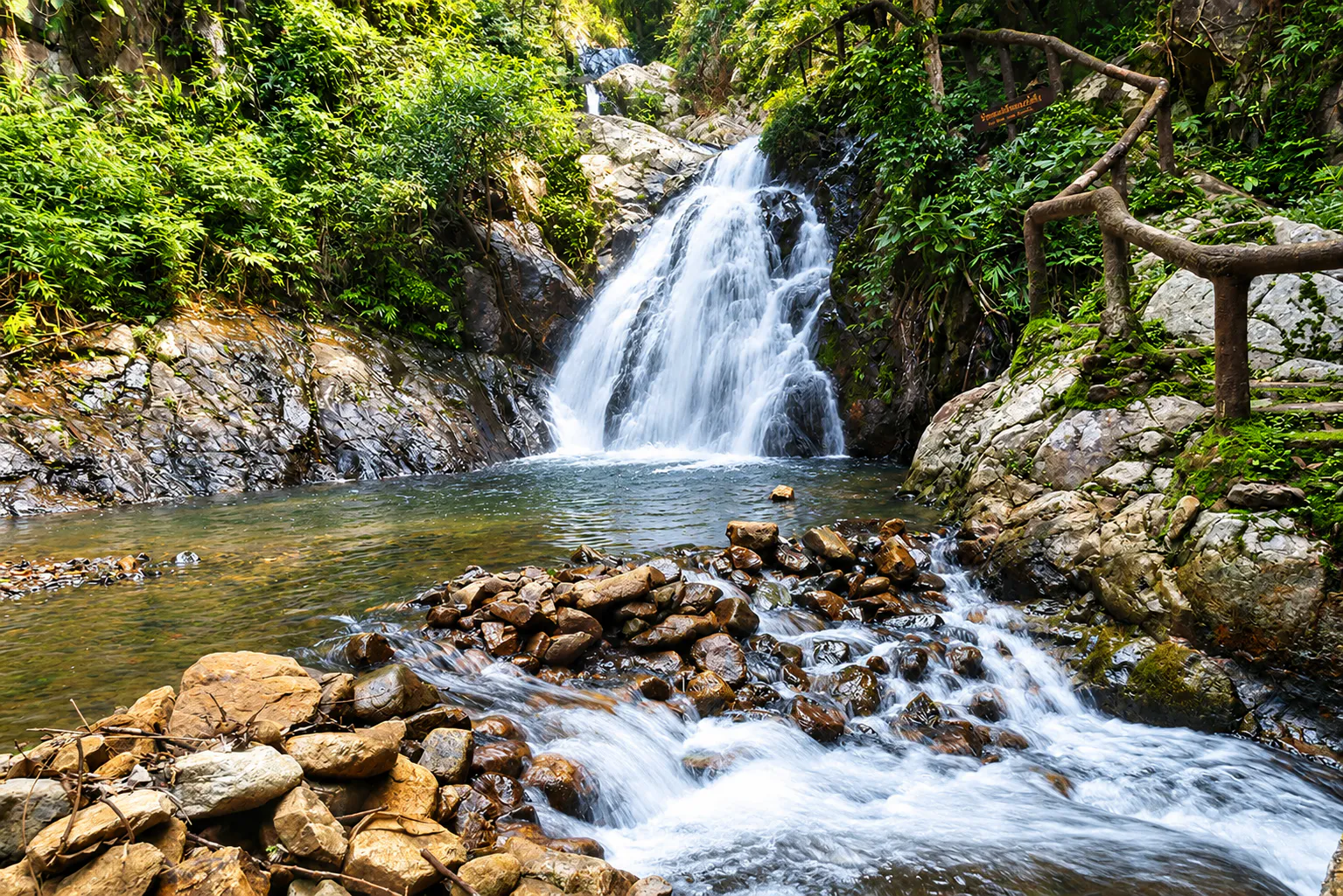 Mae Koeng Luang Waterfall cascading over dark rock through lush green forest at Wiang Kosai National Park, Phrae
