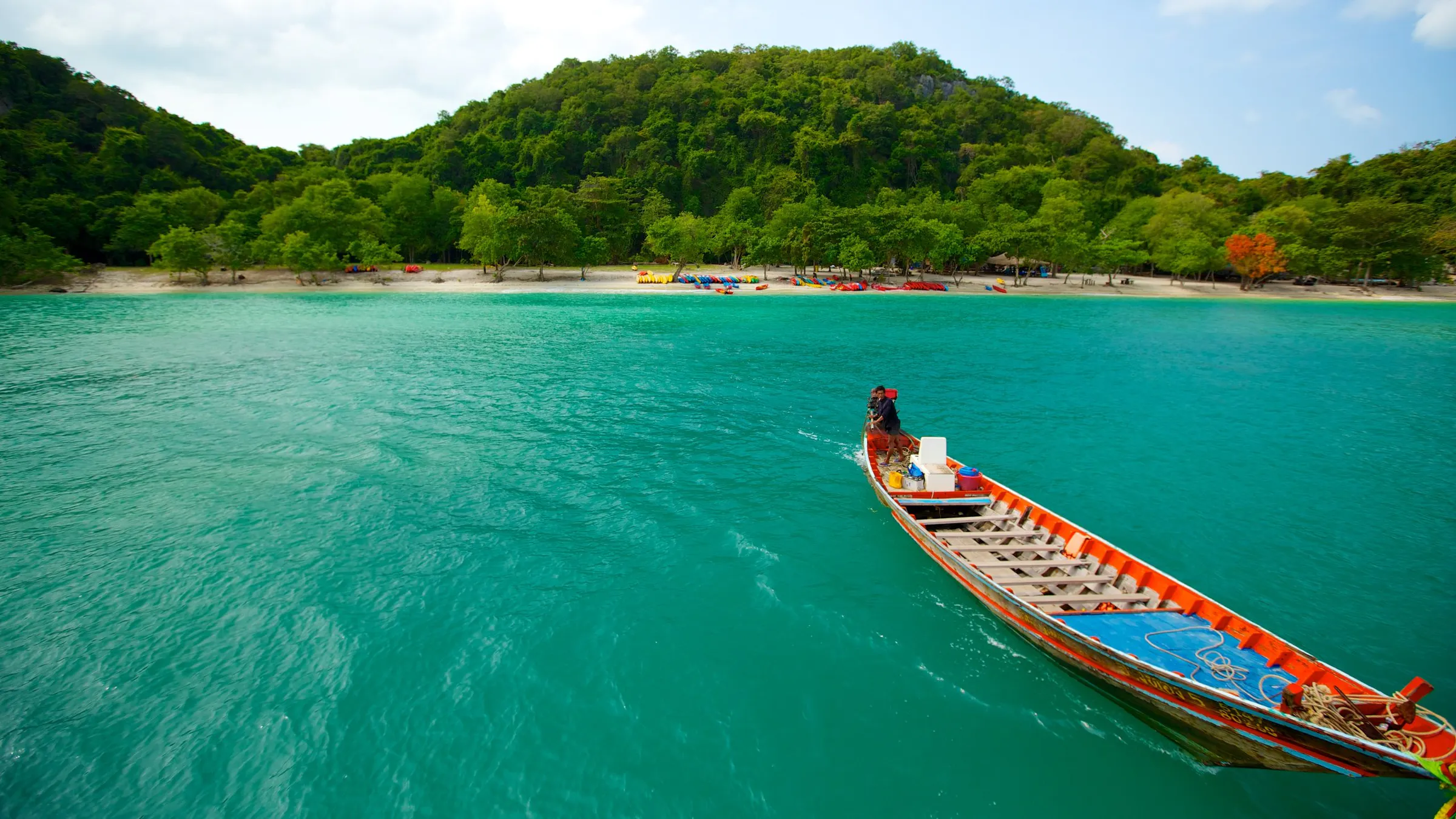 Long-tail boat cruising turquoise water toward a lush tropical island beach